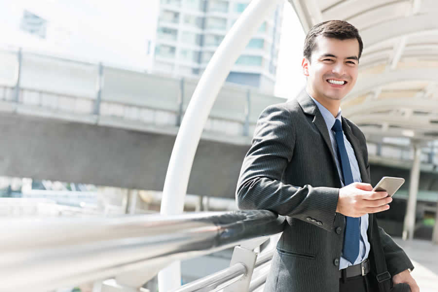 Happy smiling hispanic businessman using mobile phone outdoors in the city