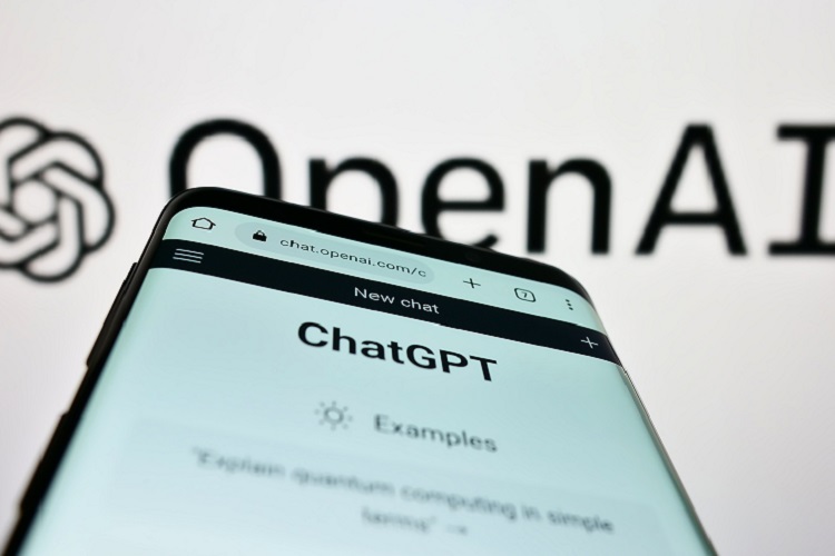 celular acessando o ChatGPT. Ao fundo, logo da OpenAI