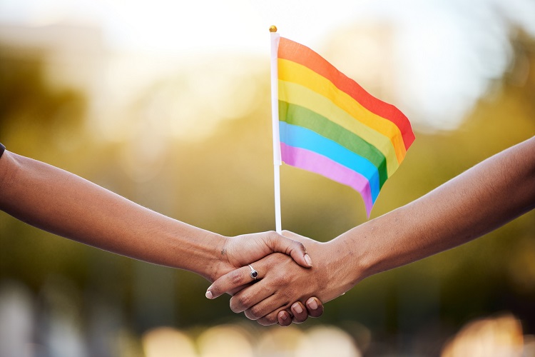 Duas pessoas de mãos dadas segurando uma bandeira LGBTQIA+